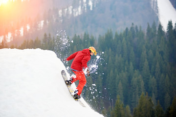 Male snowboarder in a red suit riding from the top of the snowy slope with snowboard. Skiing and snowboarding concept © anatoliy_gleb