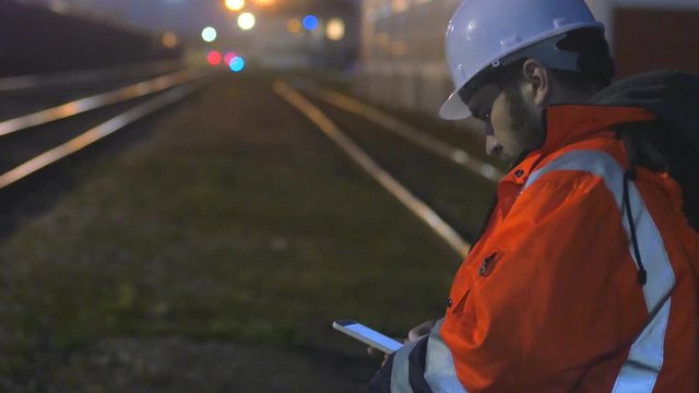 Concept of night shift. Worker in helmet using smartphone in the twilight.4k