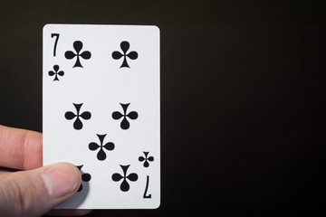 Abstract: man hand holding playing card seven of clubs on a black background with copyspace