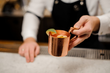 Bartender in apron presents alcoholic cocktail with ginger and lime