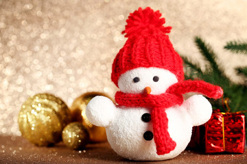 Small snowman toy with baubles and gift boxes on lights background