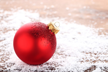 Red christmas bauble with white snow on wooden table