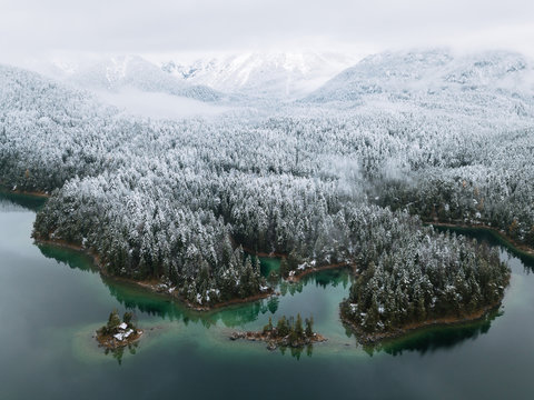 Lake Eibsee during Winter with snowy forests and calm islands in the water, Bavaria Germany