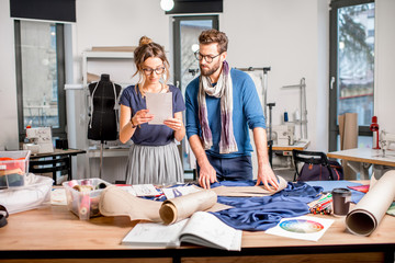 Couple of fashion designers working with fabric and clothing sketches at the studio full of...