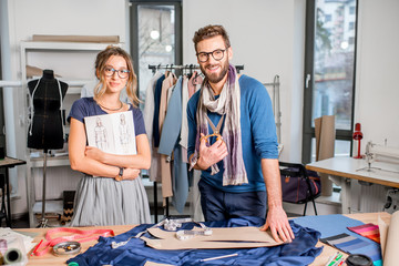 Portrait of a couple of fashion designers working with fabric and clothing sketches at the studio...