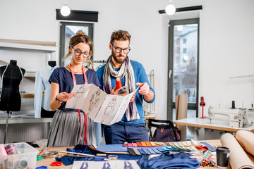 Couple of fashion designers working with clothing sketches at the studio