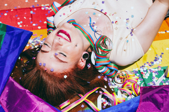 Mujer joven y pelirroja muy alegre en una fiesta y tumbada sobre una bandera arco iris 