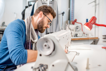 Handsome tailor sewing fabric with a sewing machine at the studio