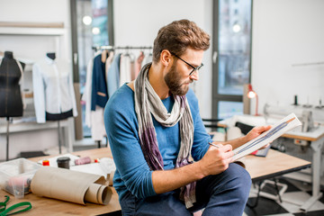 Portrait of a handsome fashion designer sitting with clothing sketches at the studio full of...