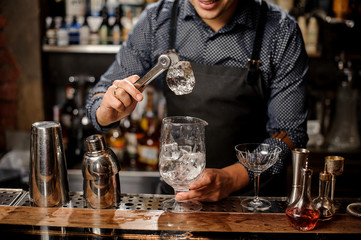 Bartender holds the piece of ice by tweezers