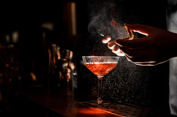 Foto op Plexiglas Cocktail Barman spuit een sinaasappelschil in cocktailglas