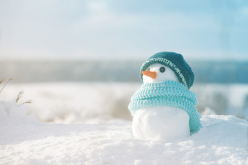Little snowman in a cap and a scarf on snow in the winter. Festive background with a lovely...