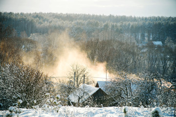 Winter evening rural landscape with houses and snow-covered roofs