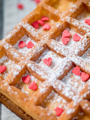 Soft Viennese Belgian waffles with powdered sugar and red hearts on rustic wooden background