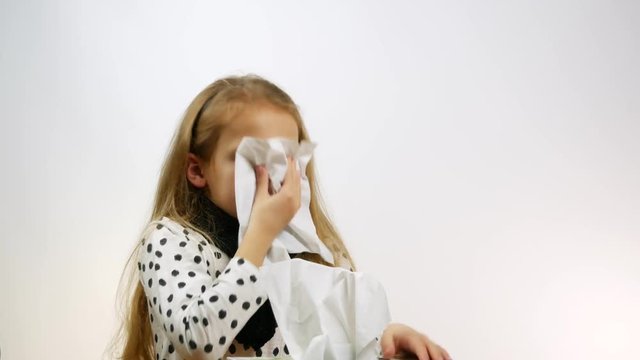 Sick caucasian girl blowing nose into tissue. Cute child suffering from rhinitis blows her nose, a studio shot.