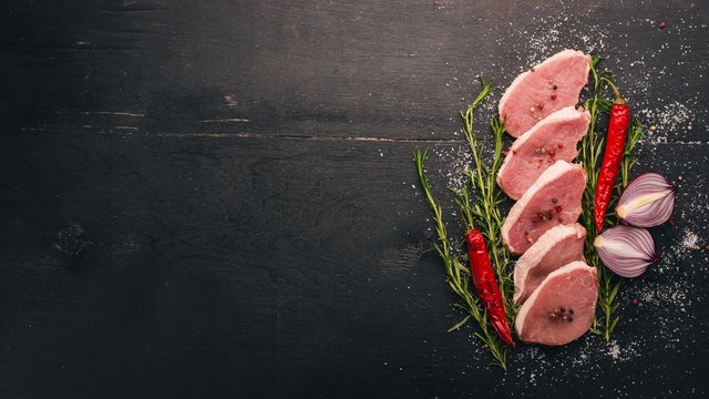 Beef steak with fresh vegetables and rosemary and spices on a black wooden background. Top view. Free space for text.