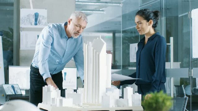 Two Professional Male and Female Architectural Engineers Work with Blueprints and on a Building Model Design for the Urban Planning Project.  Shot on RED EPIC-W 8K Helium Cinema Camera.