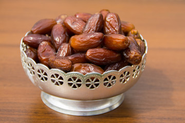 Dates fruit on a silver bowl on wooden table. The Muslim feast of the holy month of Ramadan Kareem