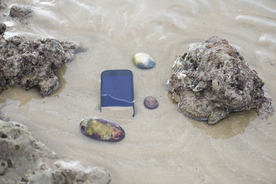 Telefono movil smartphone, arrastrado por el agua de la playa