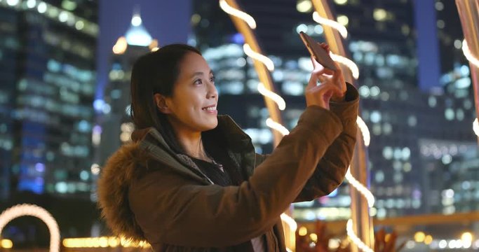 Woman using mobile phone for taking photo in the beautiful city background at night