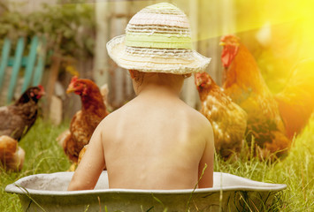 Beautiful little child girl bathing outdoors and having fun with chickens.