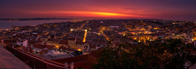 Panoramic establishing shot of Lisbon, Portugal at twilight overseeing the entire downtown, the Tagus river, the Cristo Rei and the Ponte 25 de Abril suspension bridge.