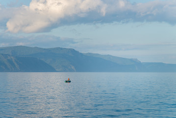 Obraz premium Boat with fisherman on Lake Baikal in calm weather . Blue sky and clouds reflection.