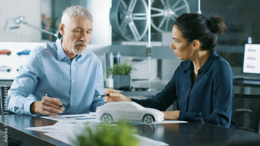 Poster experienced automotive designer and female engineer works with blueprints and sketches of a new car 