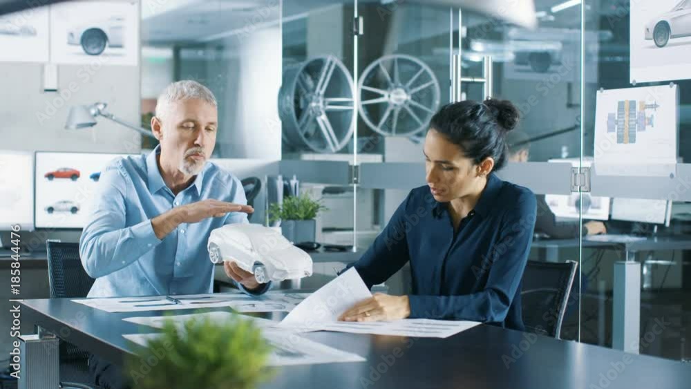 Poster experienced automotive designer and female engineer works with a concept car model prototype, perfec