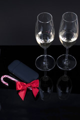 black device with a red bow and two glasses with champagne on a black background, and a Christmas candy