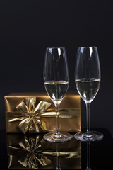 two glasses with champagne, a gift in gold paper with a bow and a carnival mask on a black background