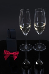 black device with a red bow and 2 glasses with champagne on a black background