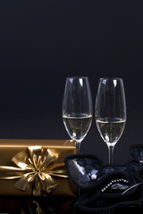 two glasses with champagne, a gift in gold paper with a bow, on a black background