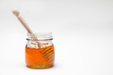 Close up of a decorative honey jar and a honey spoon on a white background with text space