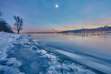 Bridge on the River Dnieper in the evening. Lantern light is reflected in the frozen ice, city