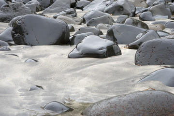 Nasse, schwarze Steine am hellen Sandstrand in den Westfjorden / Island