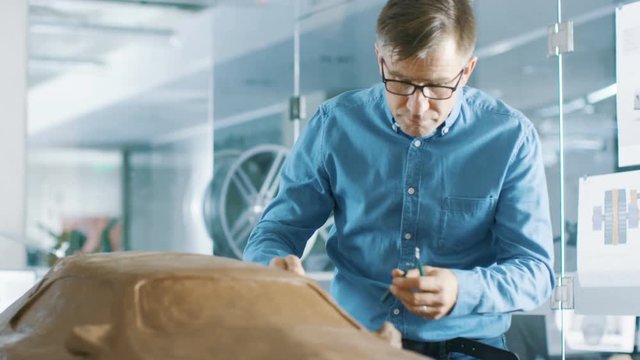 Experience Automotive Designer with a Rake Sculpts Prototype Car Model from Plasticine Clay. He Works in a Modern Studio in a Major Automotive Company's Headquarters. 
