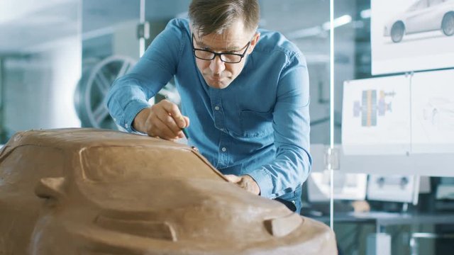 Experience Automotive Designer with a Rake Sculpts Prototype Car Model from Plasticine Clay. He Works in a Modern Studio in a Major Automotive Company's Headquarters. 