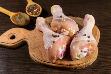Raw chicken legs with spices on wooden cutting board on a table