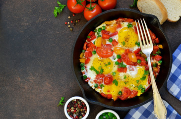 Eggs with tomatoes, pepper and green peas in a frying pan on a concrete background.