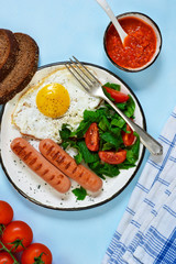 Homemade breakfast: egg, grilled sausage, vegetables, salad on a blue, concrete background.