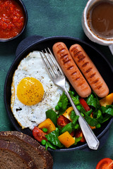 Good morning! Breakfast with sausage, egg, salad and tomato sauce with a cup of coffee on a green concrete background.