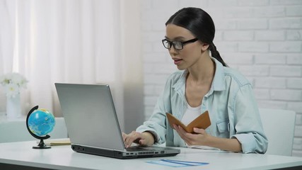 Asian girl entering passport data in laptop, booking tour at travel agency