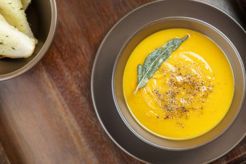 pumpkin soup with sage leaves in brown ceramic soup plate.