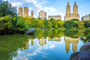 NYC skyline reflection in The Lake in Central Park. Lake on the foreground and NYC skyline on the background. Beautiful early fall hours - obrazy, fototapety, plakaty