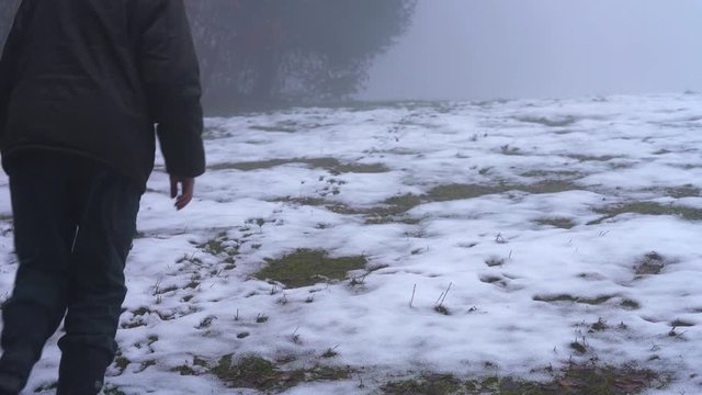 Man walking up the hill by traces in snow and goes into fog - (4K)