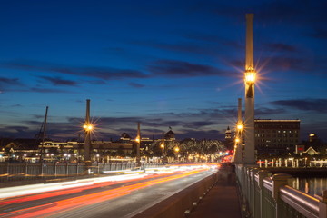City and bridge decorated with lights at twilight against blue sky showing traffic passing through shot from the bridge looking at the city