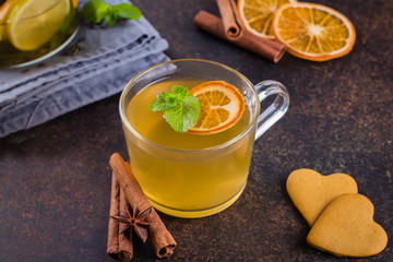 Hot Citrus Tea with orange, lemon, cinnamon, mint, anise star and carnation on dark table nbackground. Winter Healthy Cold Drink with cookies shape heart.