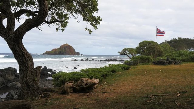 a hawaiian flag flies at koki beach, maui with alau island in the distance