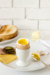 Breakfast with soft-boiled egg, bread toast, ham, cheese and canned cucumbers. Rustic style.